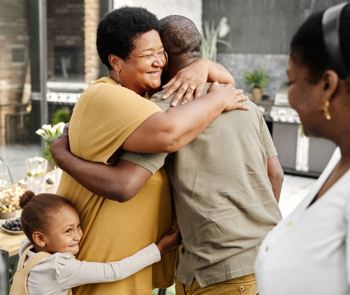 Senior woman hugging a man and smiling happily. A little girl is also hugging the woman's waist.